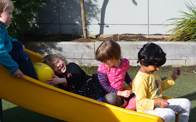 children smiling on slide at preschool