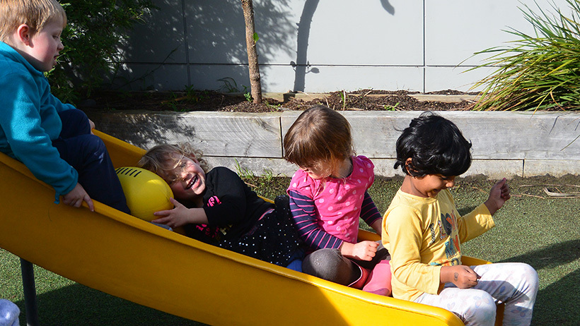 children smiling on slide at preschool