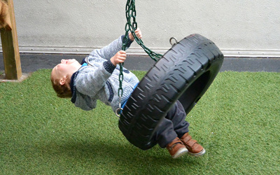 boy laughing swinging on tyre swing at daycare