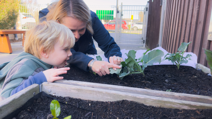A young child and a teacher exploring the gardens and natural environments at Active Explorers preschool in Rolleston